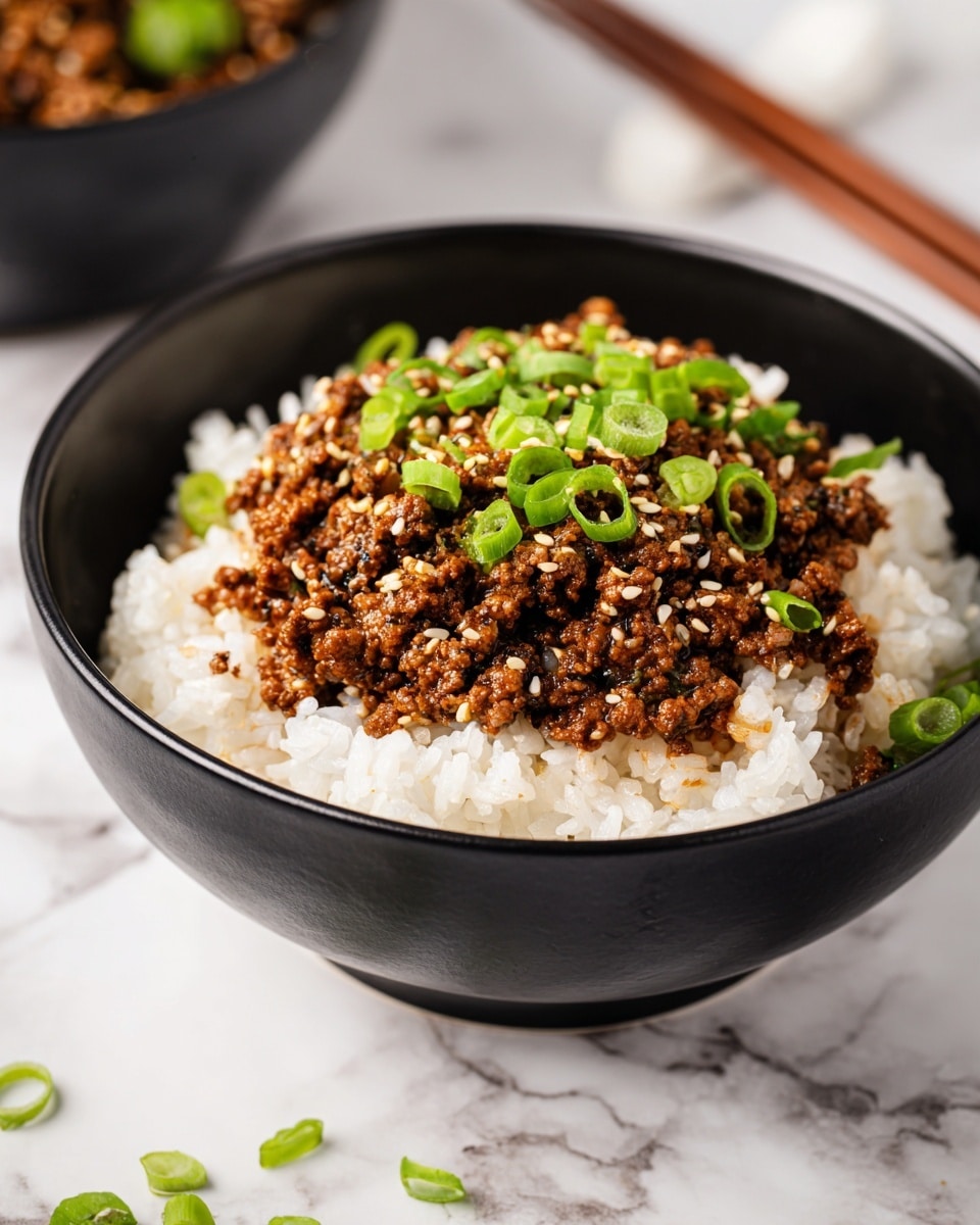 A black bowl filled with two layers: the bottom layer is white sticky rice with a soft texture, and the top layer is dark brown cooked minced meat mixed with small green chopped scallions, all sprinkled with light tan sesame seeds. The bowl is placed on a dark cloth over a white marbled surface, with a blurred pair of light-colored chopsticks and a small black bowl containing some colorful side dish in the background. photo taken with an iphone --ar 4:5 --v 7