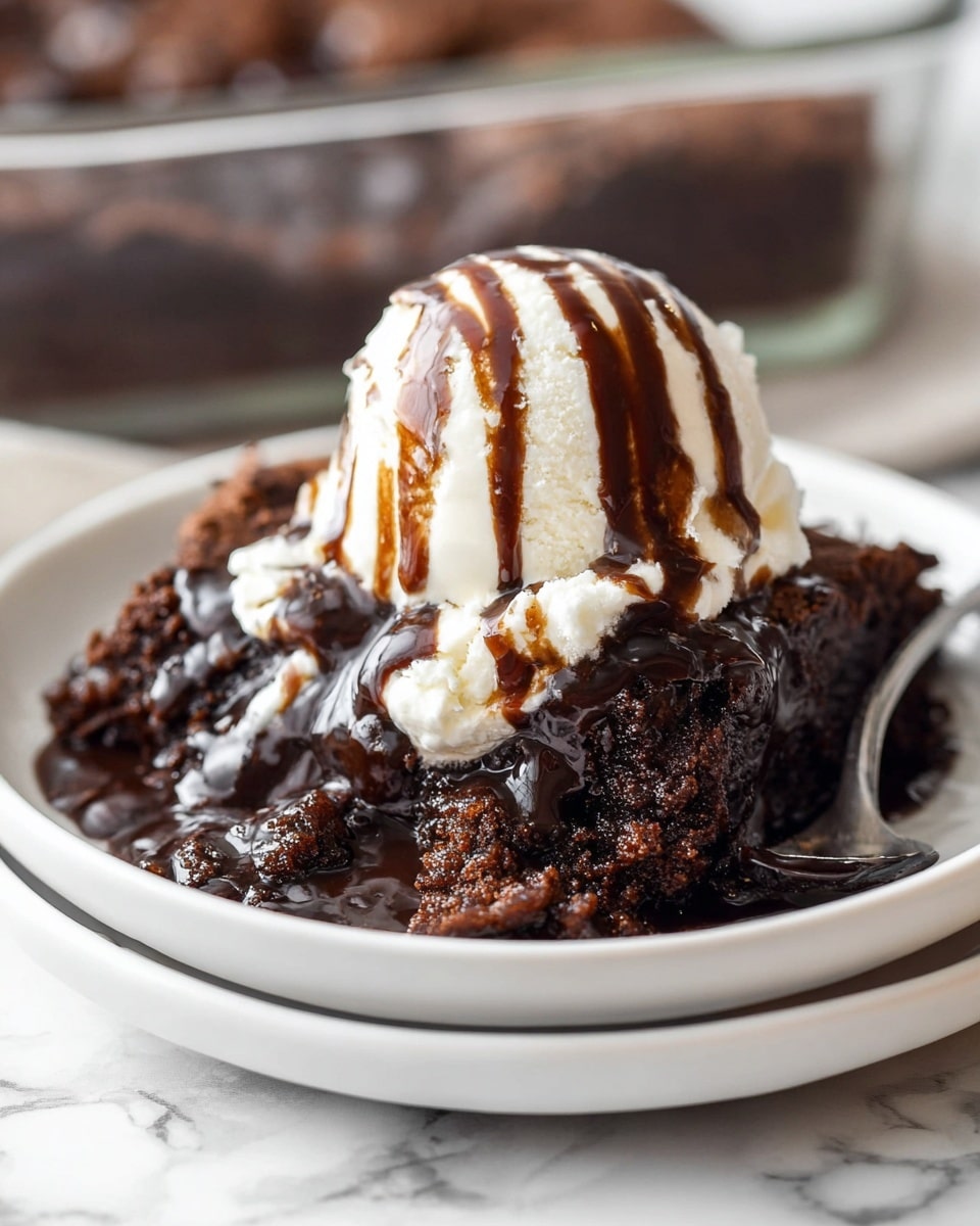 A close-up view of a dark brown, moist chocolate cake layer on a white plate that sits on top of another white plate. The cake has a shiny, thick dark chocolate sauce poured over it, creating a glossy texture. On top of the cake, there is a single scoop of creamy white vanilla ice cream, with smooth chocolate syrup drizzles running vertically over it. The plates rest on a white marbled surface, with a blurred background showing a glass baking dish. photo taken with an iphone --ar 4:5 --v 7