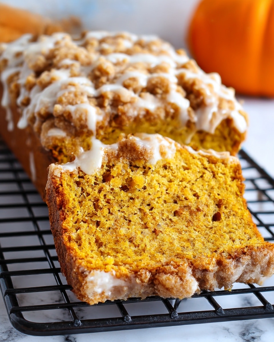 A slice of moist pumpkin bread is shown with two main layers: the bottom layer is a dense, bright orange pumpkin bread with a soft, crumbly texture, while the top layer is a thick, light brown crumb topping with a rough, chunky texture and drizzled with white icing. The bread rests on a black cooling rack placed on a white marbled surface. The background is softly blurred, with a small orange pumpkin visible, adding a cozy autumn feel. Photo taken with an iphone --ar 4:5 --v 7