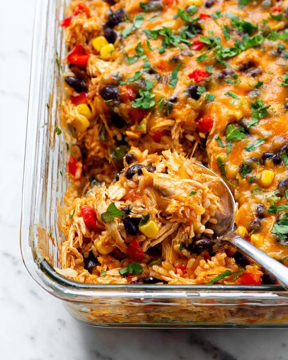A close-up view of a layered casserole in a clear glass baking dish, showing a mix of shredded chicken, black beans, cooked rice, melted cheese, red bell pepper pieces, corn kernels, and chopped green onions spread evenly throughout. The layers blend together with an orange and light brown tint from the sauce and cheese, topped with fresh green herbs. A spoon rests in the dish, scooping a portion, with the food appearing warm and cheesy. The dish is set on a white marbled surface. photo taken with an iphone --ar 4:5 --v 7