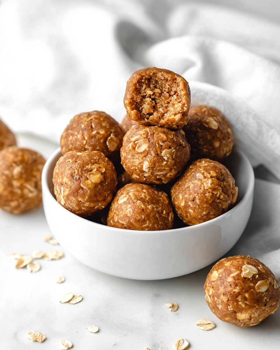 A white round bowl filled with about ten medium-sized energy balls stacked on top of each other. Each ball is light brown with visible oats mixed in, giving a rough texture. Some energy balls are also placed around the bowl on a white marbled surface, and a white cloth is softly draped behind the bowl. The background shows white tiled walls with clear, straight lines. photo taken with an iphone --ar 4:5 --v 7