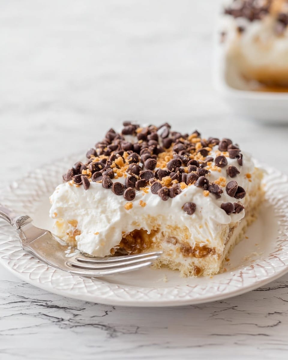 A square dessert in a white foil-lined pan with four visible layers: a bottom crumbly light brown crust, a thick orange layer above it, followed by a thick white creamy layer, and topped with a dense layer of small dark brown chocolate chips and tiny light tan crunchy bits scattered evenly. Part of one corner has been cut out showing the layers clearly, and a silver spoon rests inside the pan with some white cream on it. The pan sits on a white marbled surface. Photo taken with an iphone --ar 4:5 --v 7