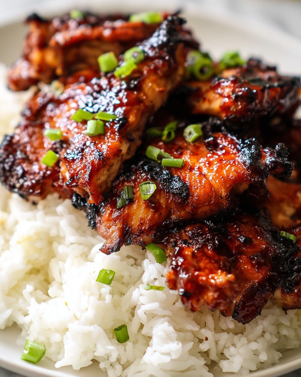 This dish shows a close-up of a single layer of grilled chicken pieces with a rich, dark glazed surface that looks shiny and slightly charred, placed on top of a base layer of fluffy white rice. The chicken has a reddish-brown color with blackened edges, showing a smoky texture. Small pieces of bright green chopped scallions are scattered on both the chicken and rice, adding a fresh contrast. The food sits on a white plate with a white marbled background. photo taken with an iphone --ar 4:5 --v 7